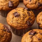 Close-up of freshly baked banana chocolate chip muffins in brown paper liners, topped with chunks of melted chocolate