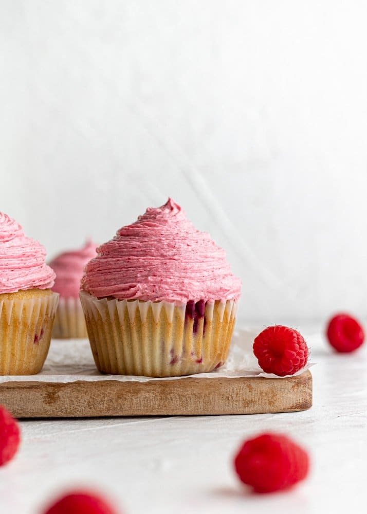raspberry cupcake with raspberries scattered around it