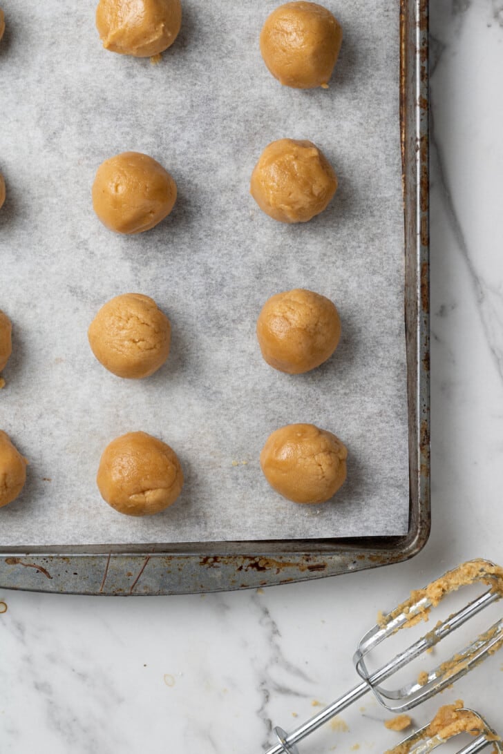 balls of peanut butter cookie dough on a parchment lined baking sheet before baking.
