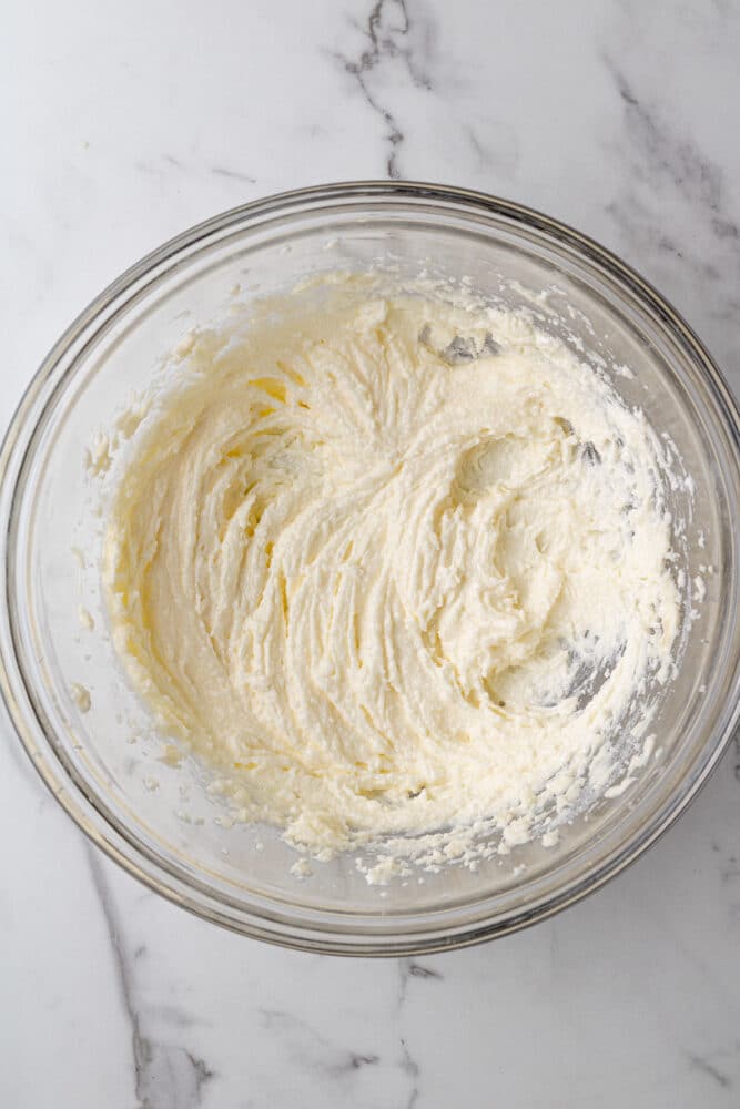 butter and sugar mixed together in a glass bowl on a marble countertop.