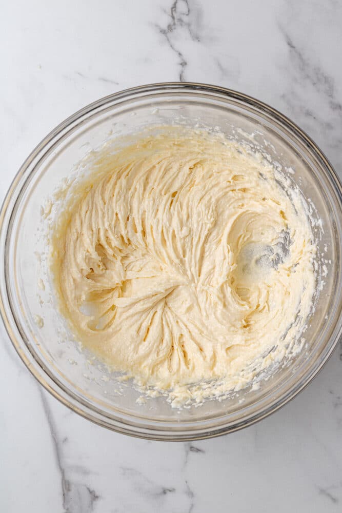 sugar, butter, vanilla, and egg mixed in a glass bowl on a marble countertop.