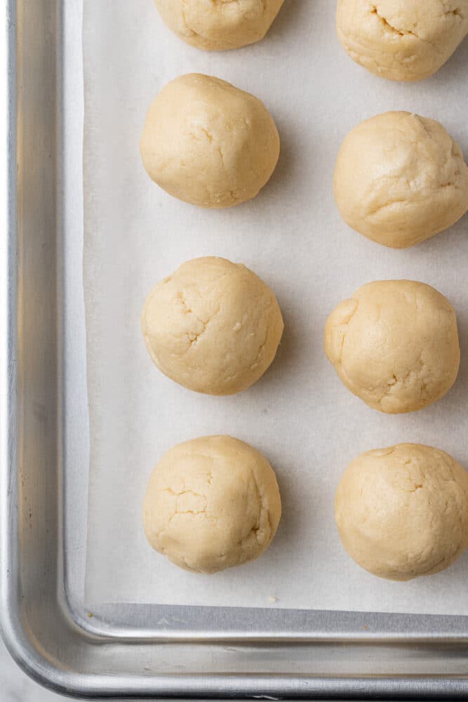 Eight balls of cookie dough on a parchment lined baking pan.