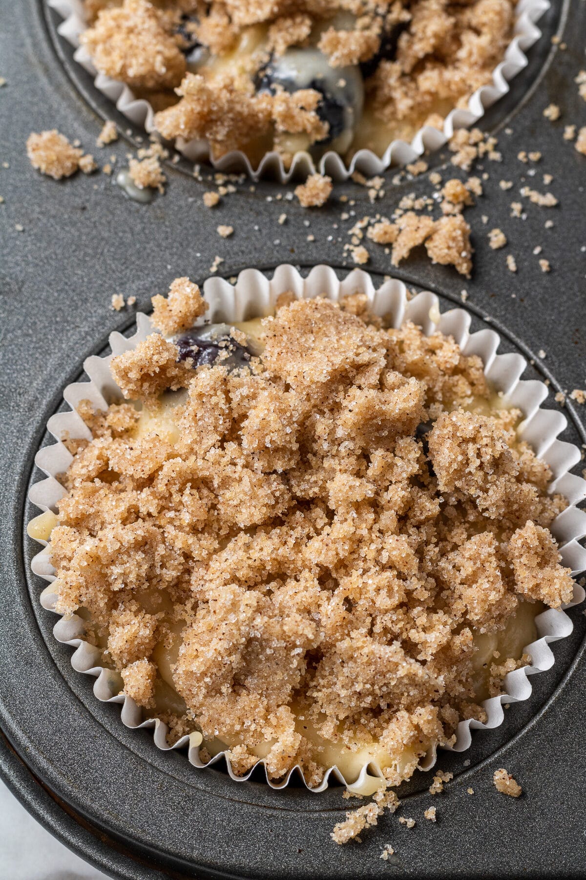 blueberry muffin batter in a muffin tin with cinnamon streusel on top
