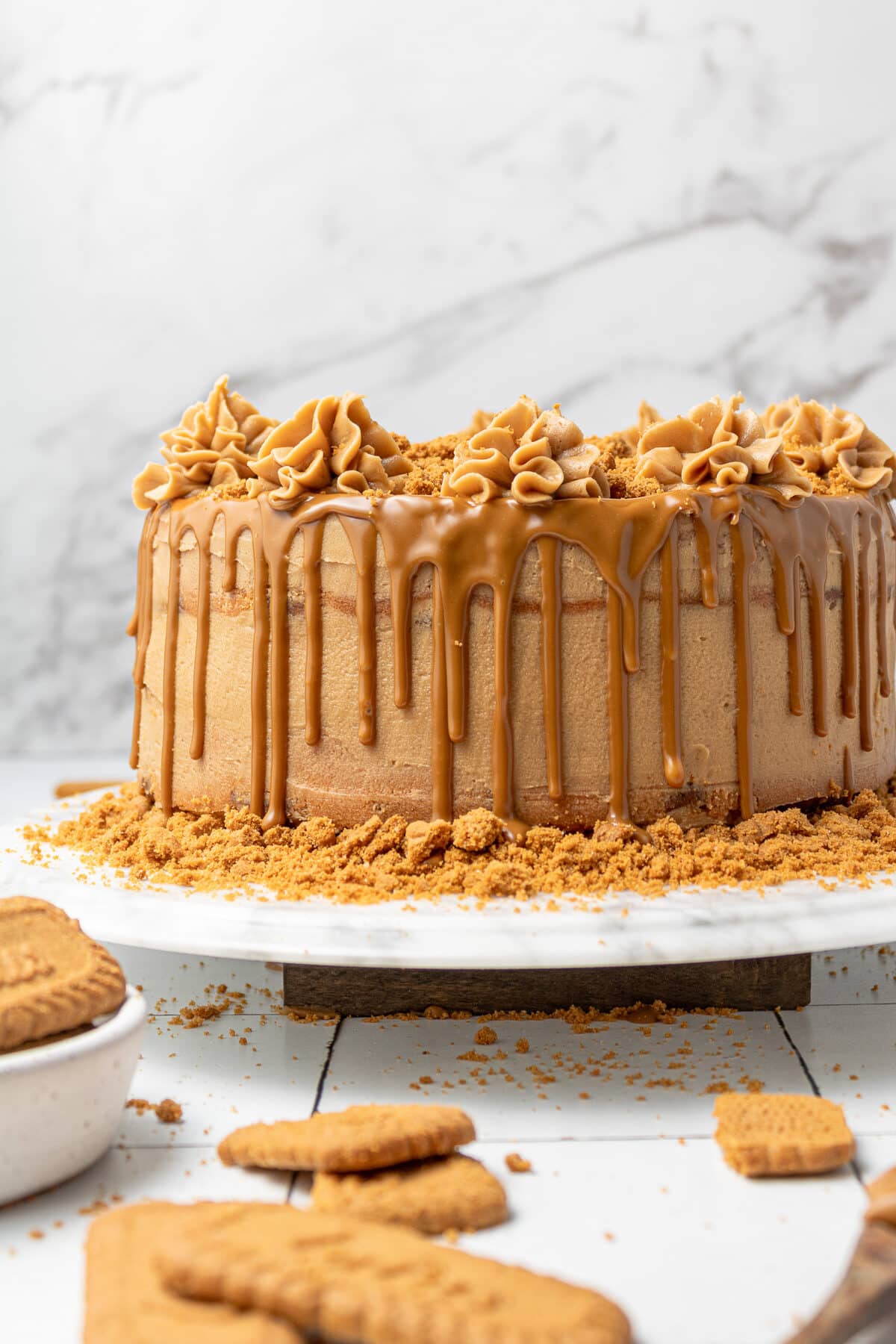 biscoff cake on a cake stand with biscoff cookies scattered around it