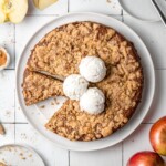 vegan apple cake on a plate with vegan ice cream on top and bits of crumble around it