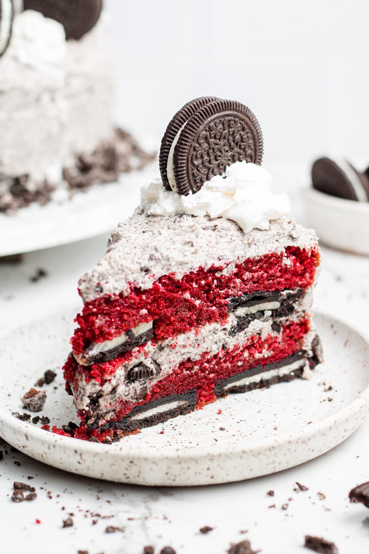 Plated piece of Oreo red velvet cake. Pieces of Oreo scattered around