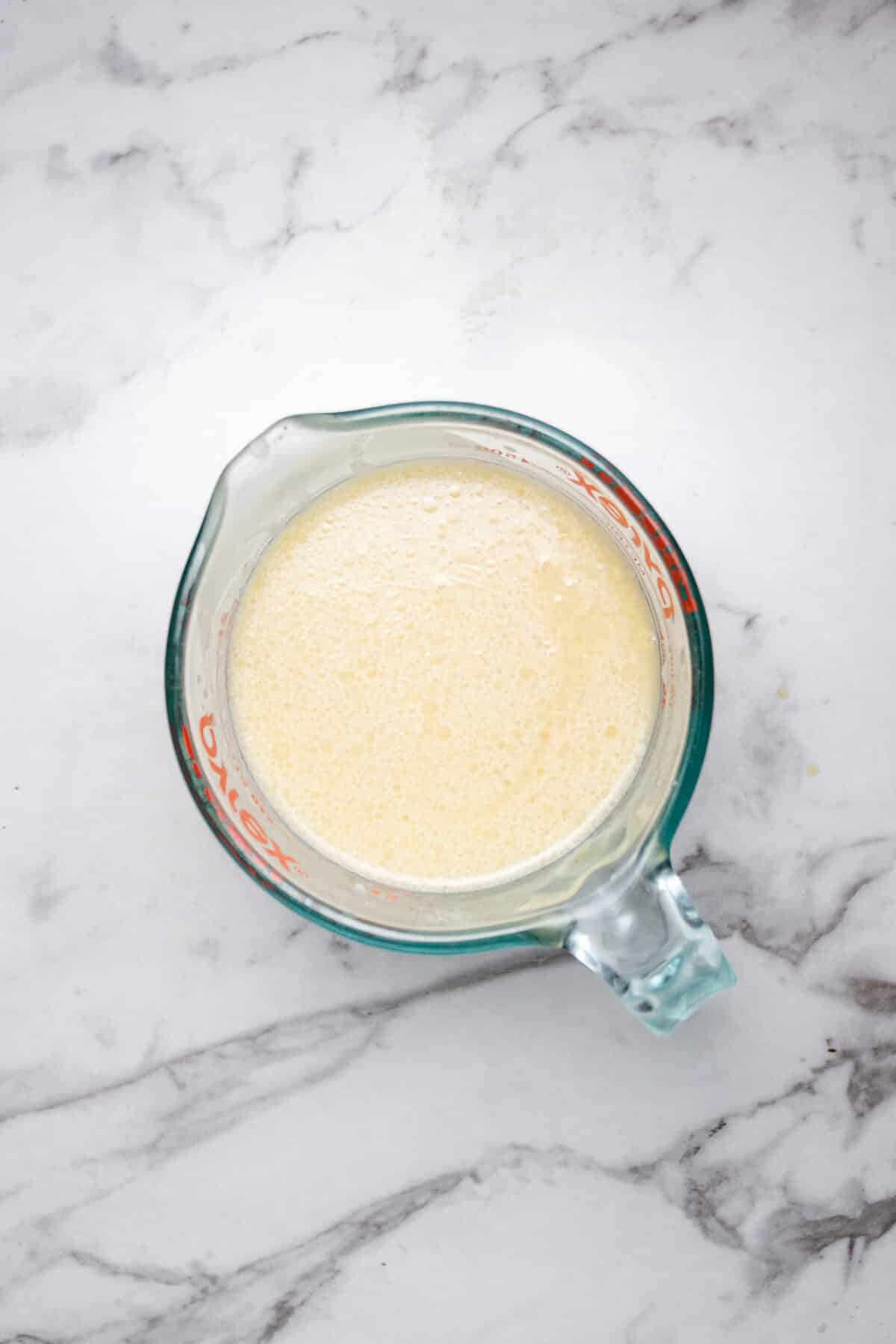 wet ingredients mixed together in a glass measuring cup on a marble countertop.