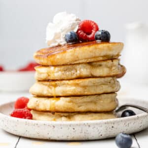 Stack of 5 dairy free oat milk pancakes plated with berries scattered around