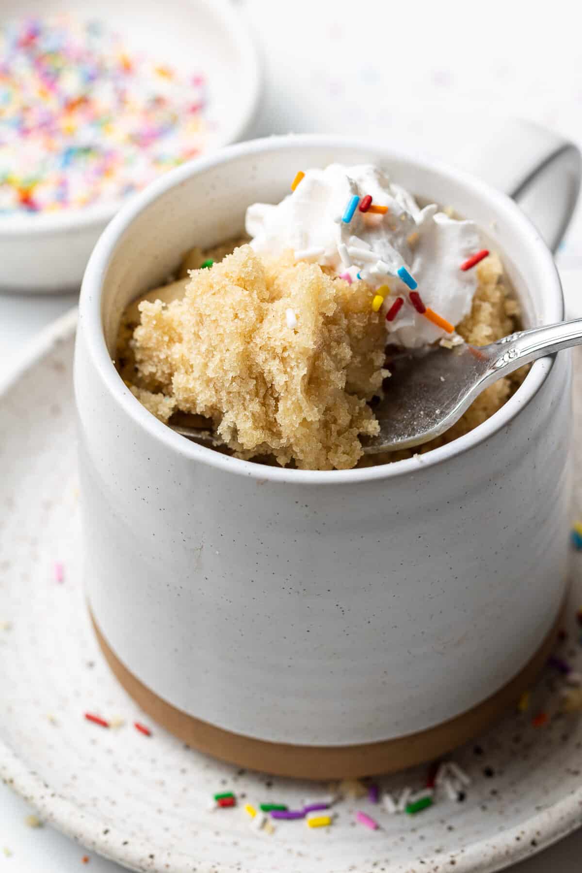 Vegan vanilla mug cake with sprinkles in a large mug with a fork scooping the cake
