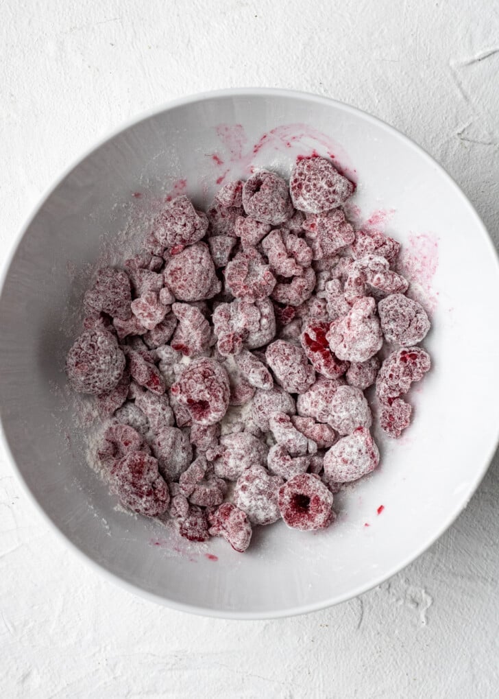 frozen raspberries covered in flour in a white glass bowl.