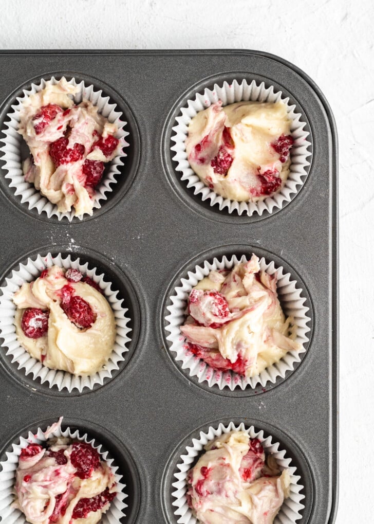 six raspberry cupcake batter in paper liners in an aluminium cupcake tin.