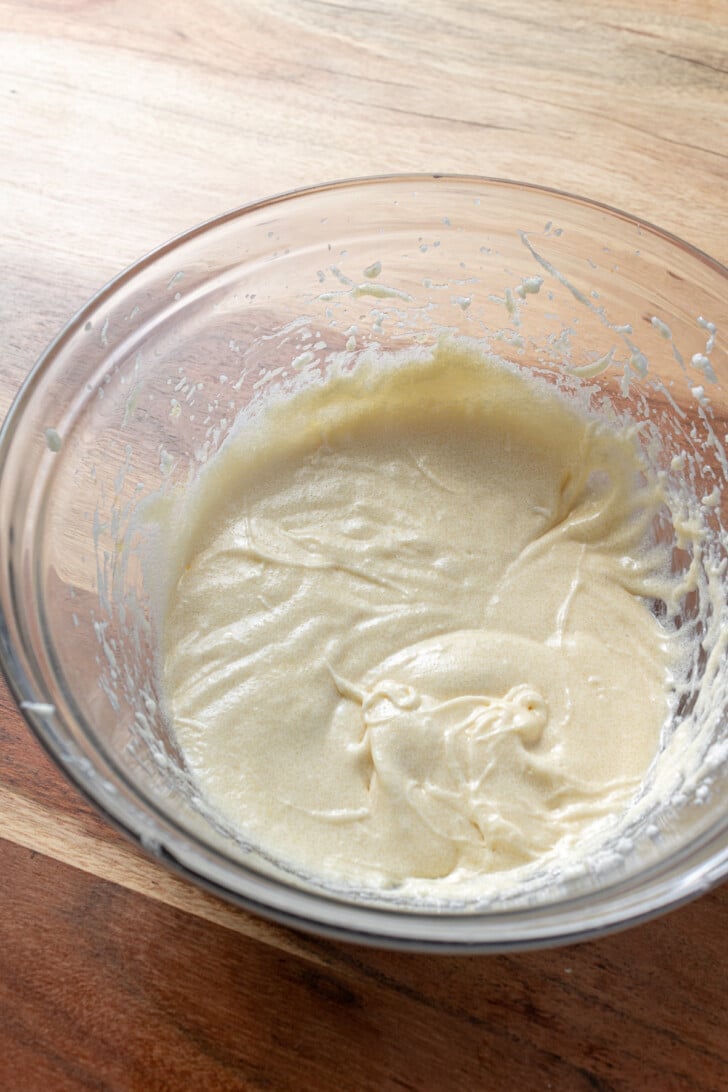 wet ingredients mixed together in a glass mixing bowl on a wooden countertop.