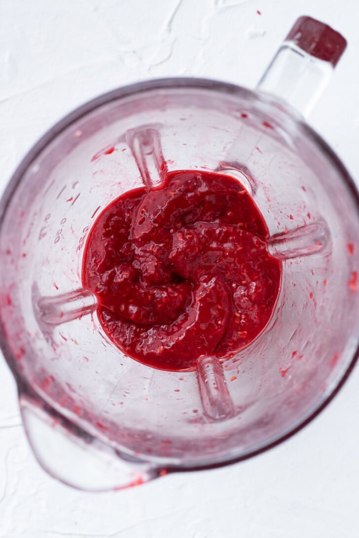 raspberries pureed in a glass blender on a white countertop.