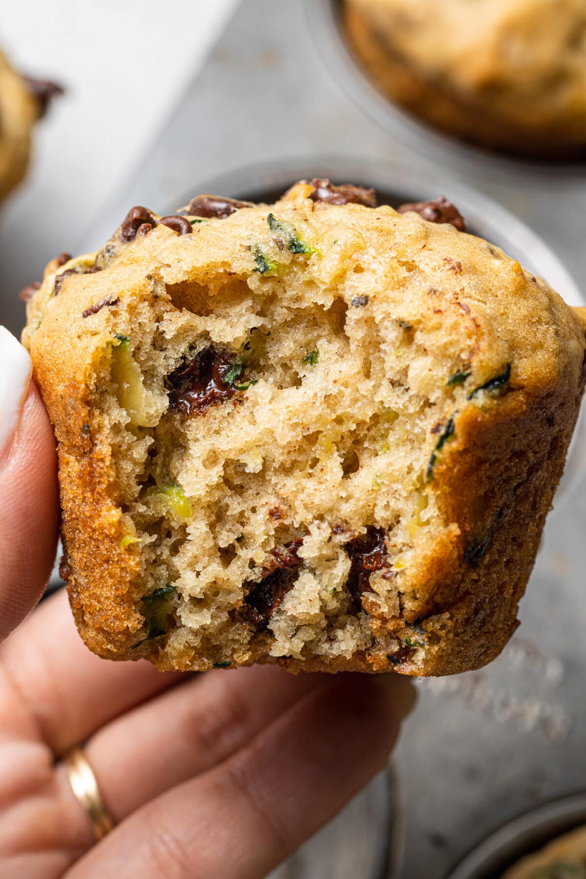 hand holding a vegan zucchini muffin with a bite out of it
