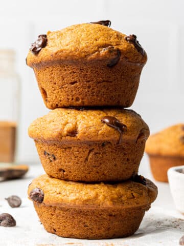 Three vegan pumpkin muffins stacked with chocolate chips scattered around