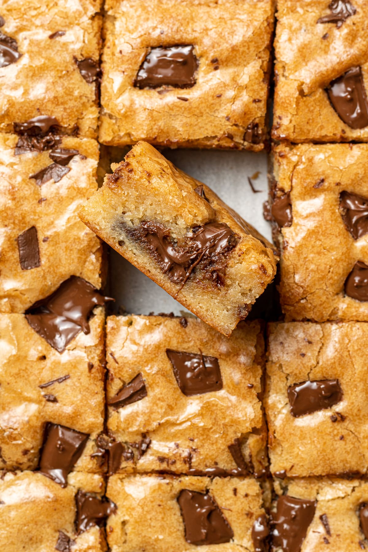 blonde brownies on parchment paper sliced into squares with one blondie facing upwards
