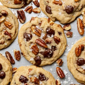Baking sheet of chocolate chip pecan cookies. Cookies are loaded with pecans and chocolate chips with pecans scattered around