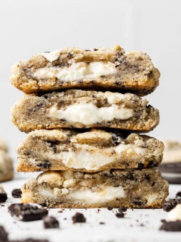 Four stacked oreo cheesecake cookies broken in half so you can see the cream cheese inside