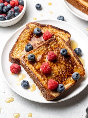 Two slices of healthy french toast plated and topped with blueberries and raspberries