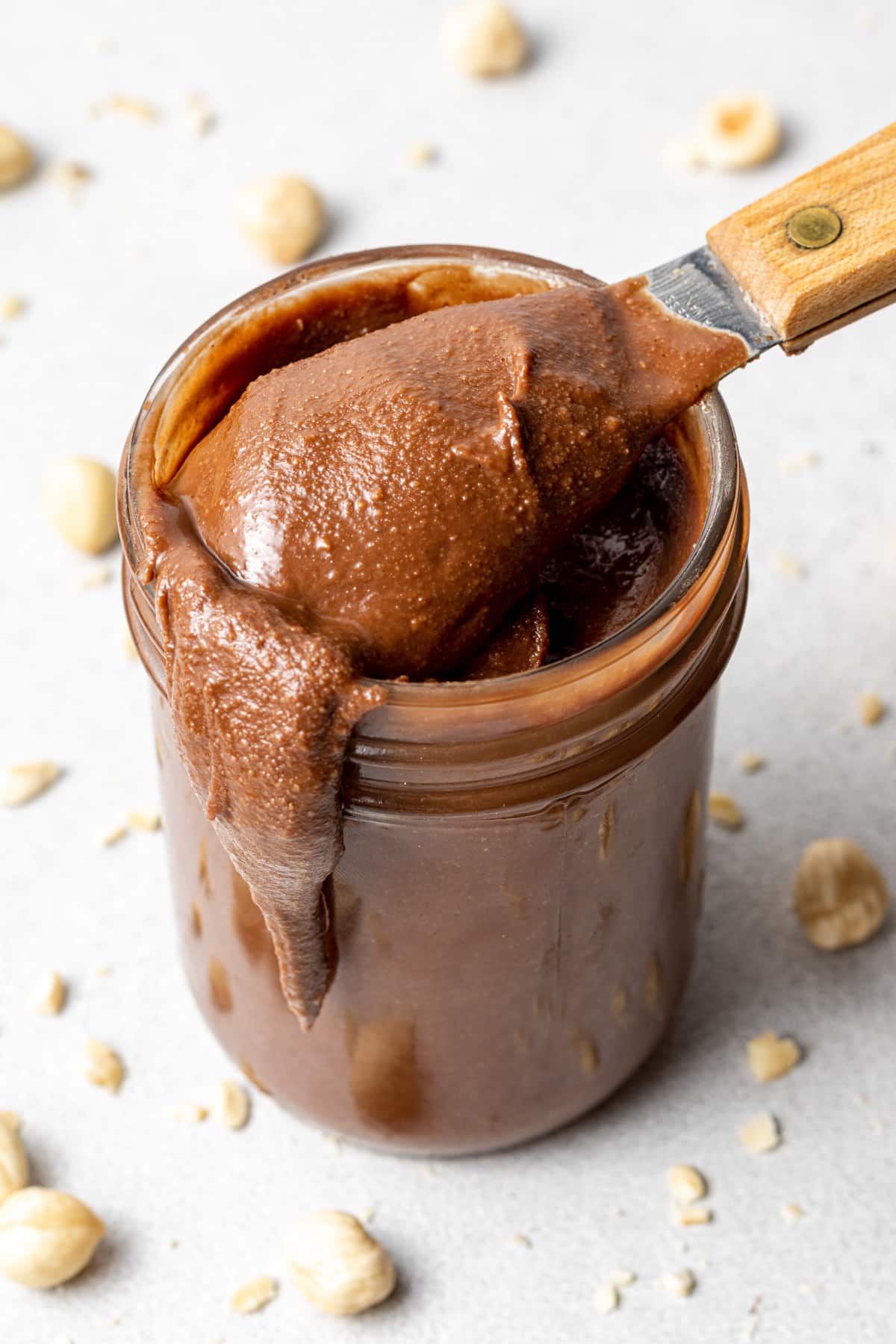 a jar of vegan nutella with a spoonful coming out and hazelnuts scattered around