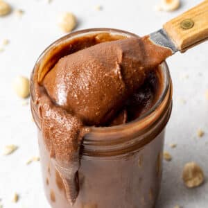 a jar of vegan nutella with a spoonful coming out and hazelnuts scattered around