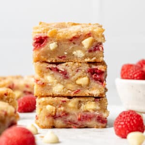 Three White Chocolate Raspberry Blondie squares stacked with raspberries around