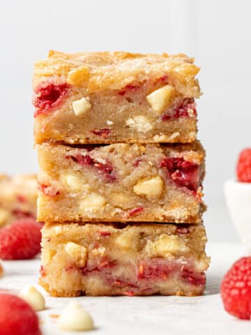 Three White Chocolate Raspberry Blondie squares stacked with raspberries around