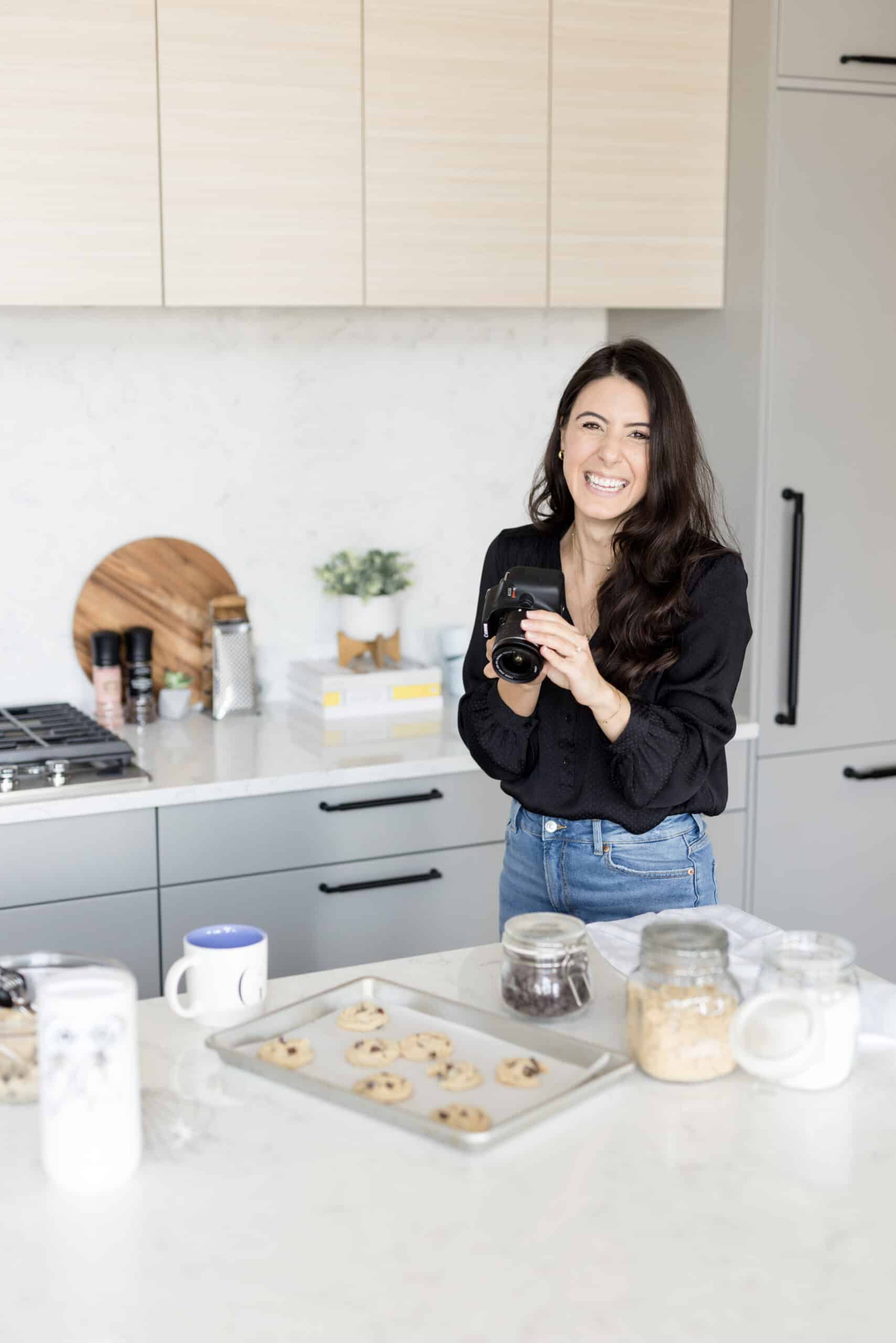 a food blogger in a kitchen holding a camera and taking photos of chocolate chip cookies
