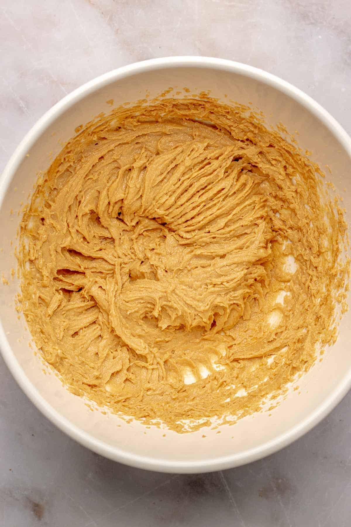 peanut butter and butter mixed together in a white bowl on a marble countertop.