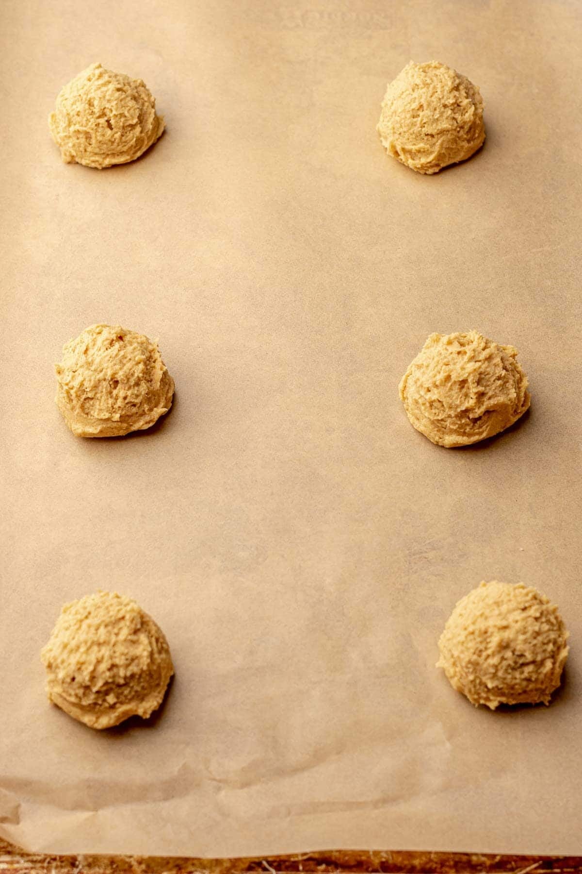 six balls of peanut butter cookie dough on a parchment lined baking sheet.