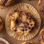 Close-up of chocolate-swirl muffins on a brown surface. One muffin is cut open, revealing a rich chocolate center. A swirl of chocolate in a bowl is visible.
