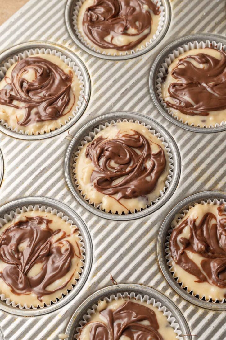 Cupcake pan with nine unbaked swirl muffins, featuring a marbled chocolate and vanilla pattern, creating a homemade, inviting feel.