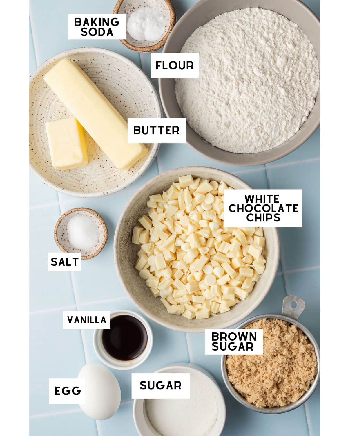 ingredients for making cookies in small bowls on a blue tiled backdrop.