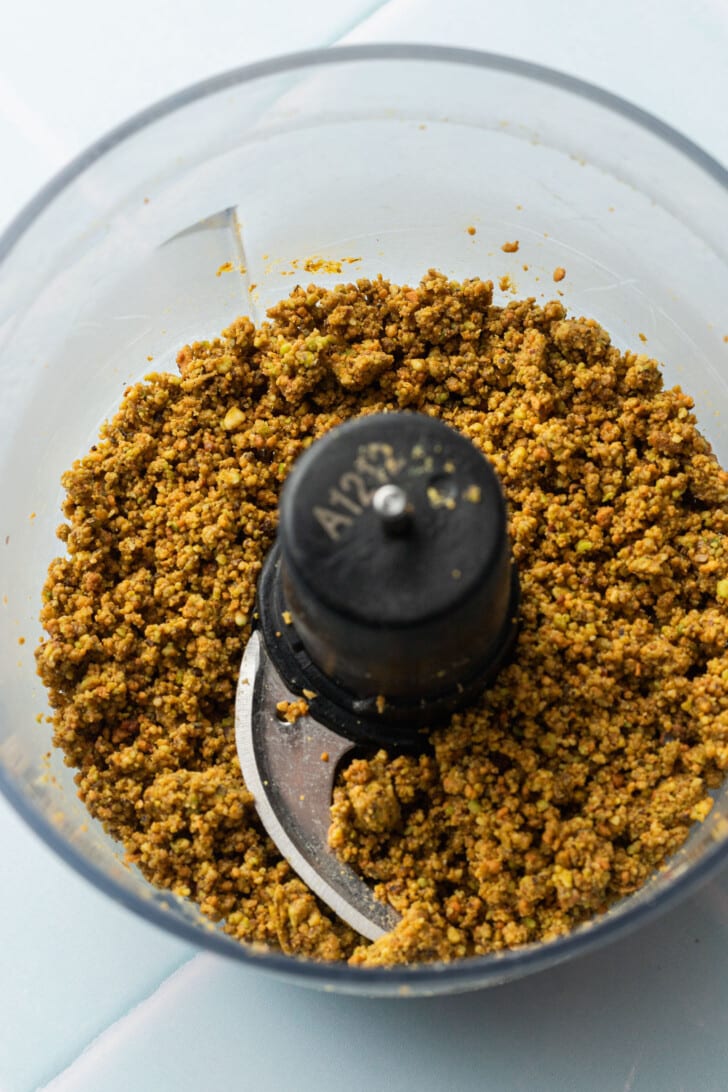 A food processor bowl filled with finely ground, pistachios