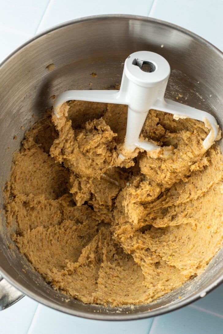 Thick, creamy dough in a metal mixer bowl with a white paddle attachment, ready for baking, conveying a sense of warmth and anticipation.