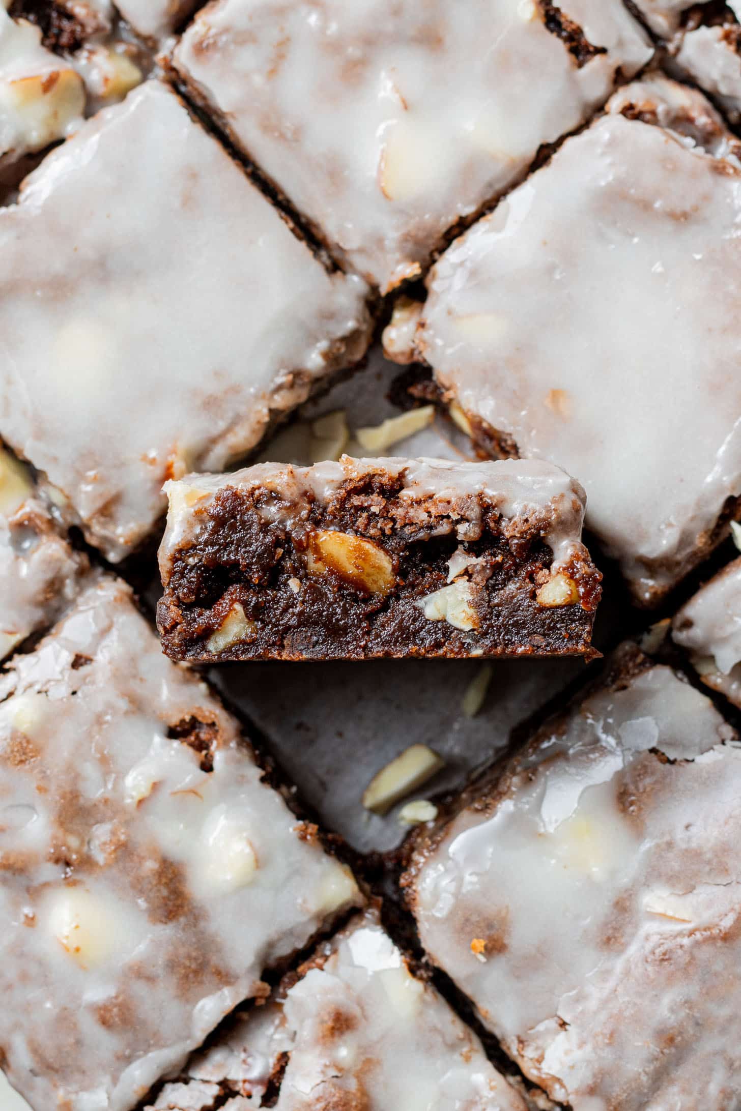 Close-up of glazed brownies cut into squares, with one piece turned to reveal a rich, chocolate interior with visible nuts, conveying a tempting sweetness.