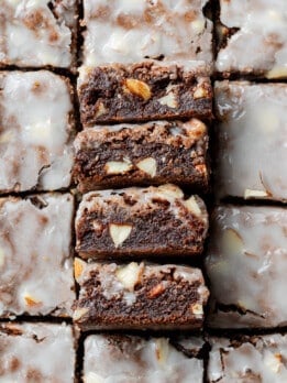 Close-up of glazed brownies cut into squares. The rich, chocolatey texture features visible nuts.