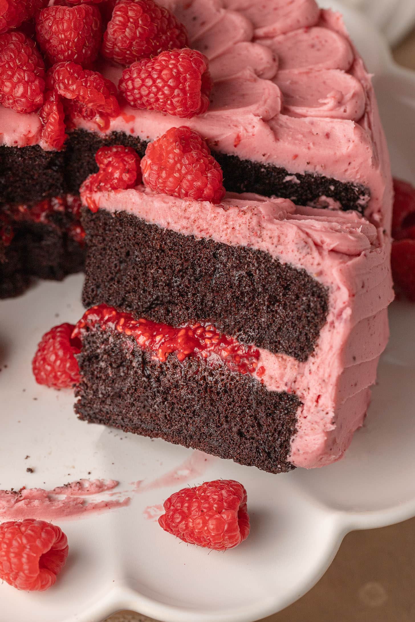 A chocolate cake with two layers of dark sponge and vibrant pink raspberry frosting. Fresh raspberries garnish the top. A slice is removed, exposing the rich texture.