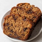 Three slices of moist banana bread with chocolate chips on a white, speckled plate. The bread appears soft and rich, creating a warm, inviting feel.