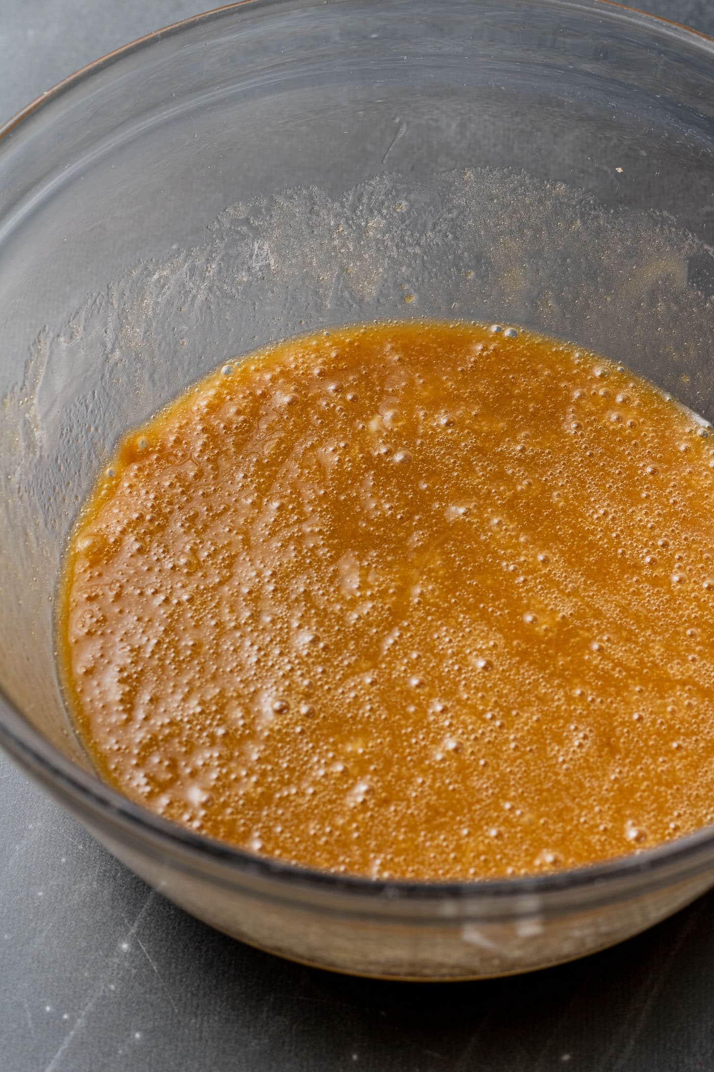 A glass bowl containing a smooth, caramel-colored batter sits on a dark surface. The rich texture suggests a sweet and inviting dessert mix.
