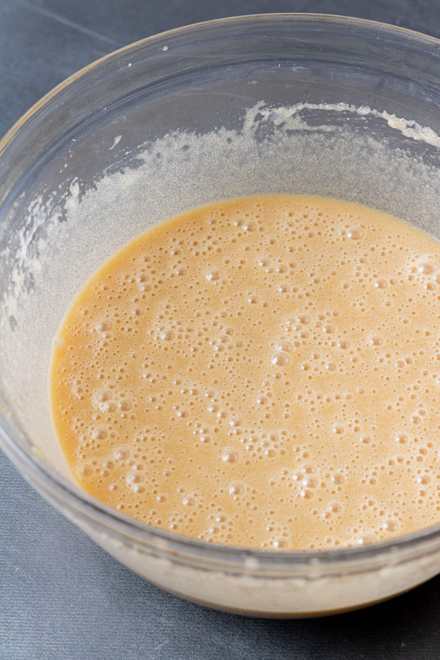 A large glass bowl filled with smooth, bubbly beige batter against a dark surface, conveying a feeling of anticipation for baking.