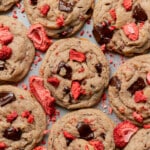 Close-up of freshly baked cookies with dark chocolate chunks and vibrant red dried strawberries, scattered in an inviting pattern on a tray.