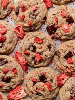 Close-up of freshly baked cookies with dark chocolate chunks and vibrant red dried strawberries, scattered in an inviting pattern on a tray.