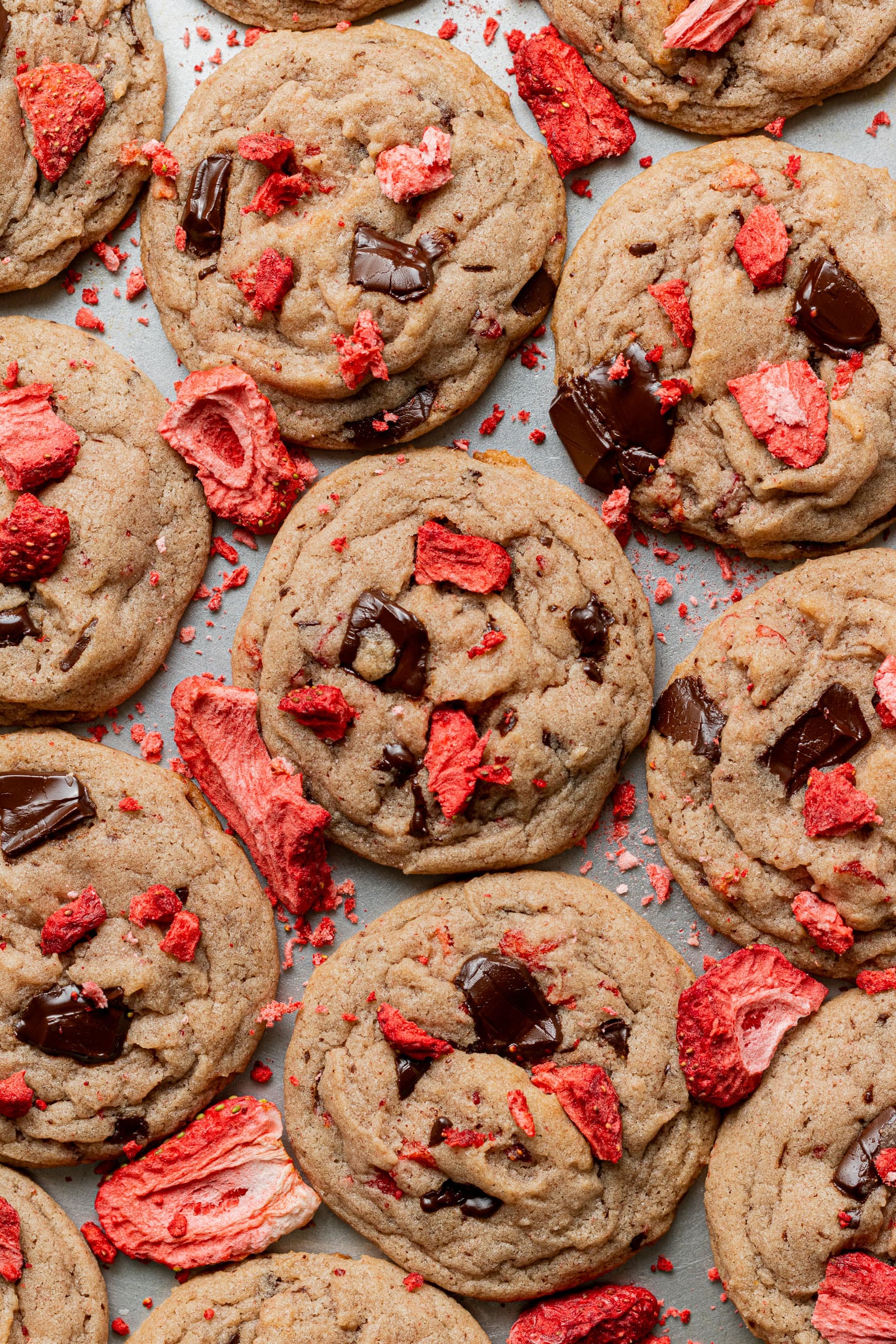 Close-up of freshly baked cookies with dark chocolate chunks and vibrant red dried strawberries, scattered in an inviting pattern on a tray.