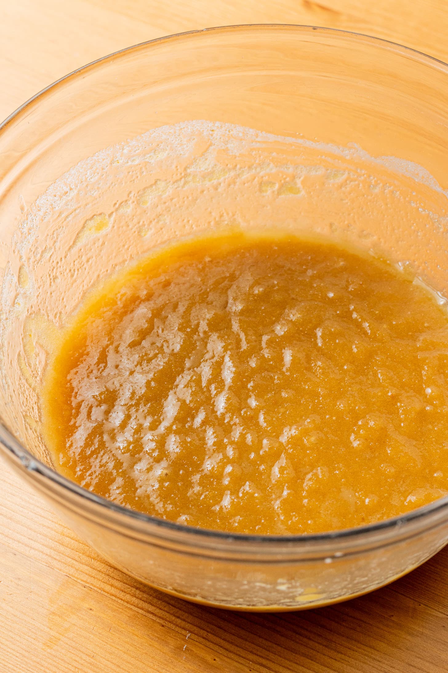 A glass bowl on a wooden surface containing thick, smooth, golden pumpkin batter. The mixture appears slightly textured, suggesting readiness for baking.