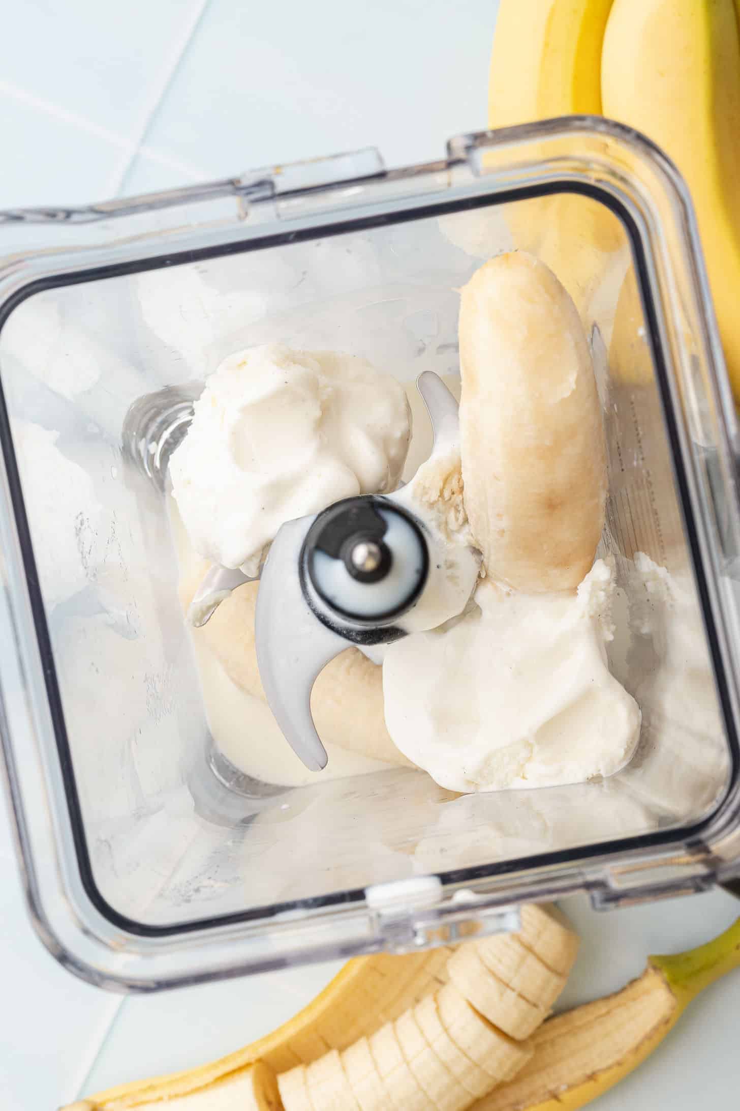 Overhead view of banana pieces and scoops of vanilla ice cream loaded into a blender, ready to blend into a milkshake