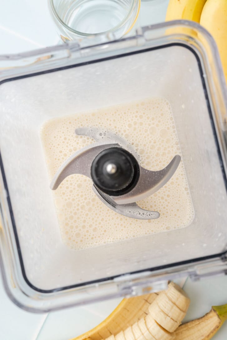 Overhead view of a smooth, frothy blended banana milkshake in a blender, ready to pour