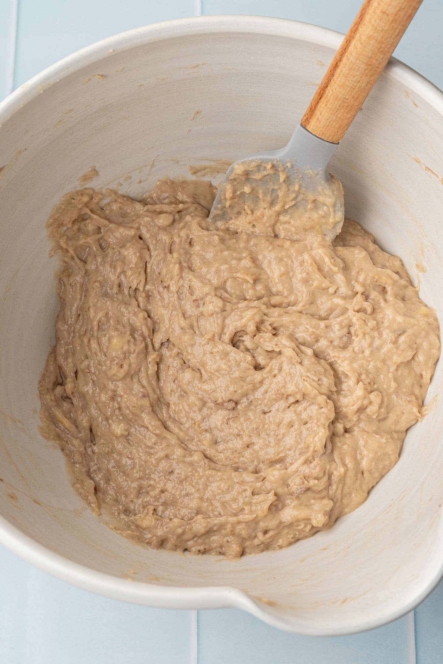 Overhead view of thick banana muffin batter folded together in a large white ceramic bowl with a rubber spatula, ready to be portioned into a muffin tin