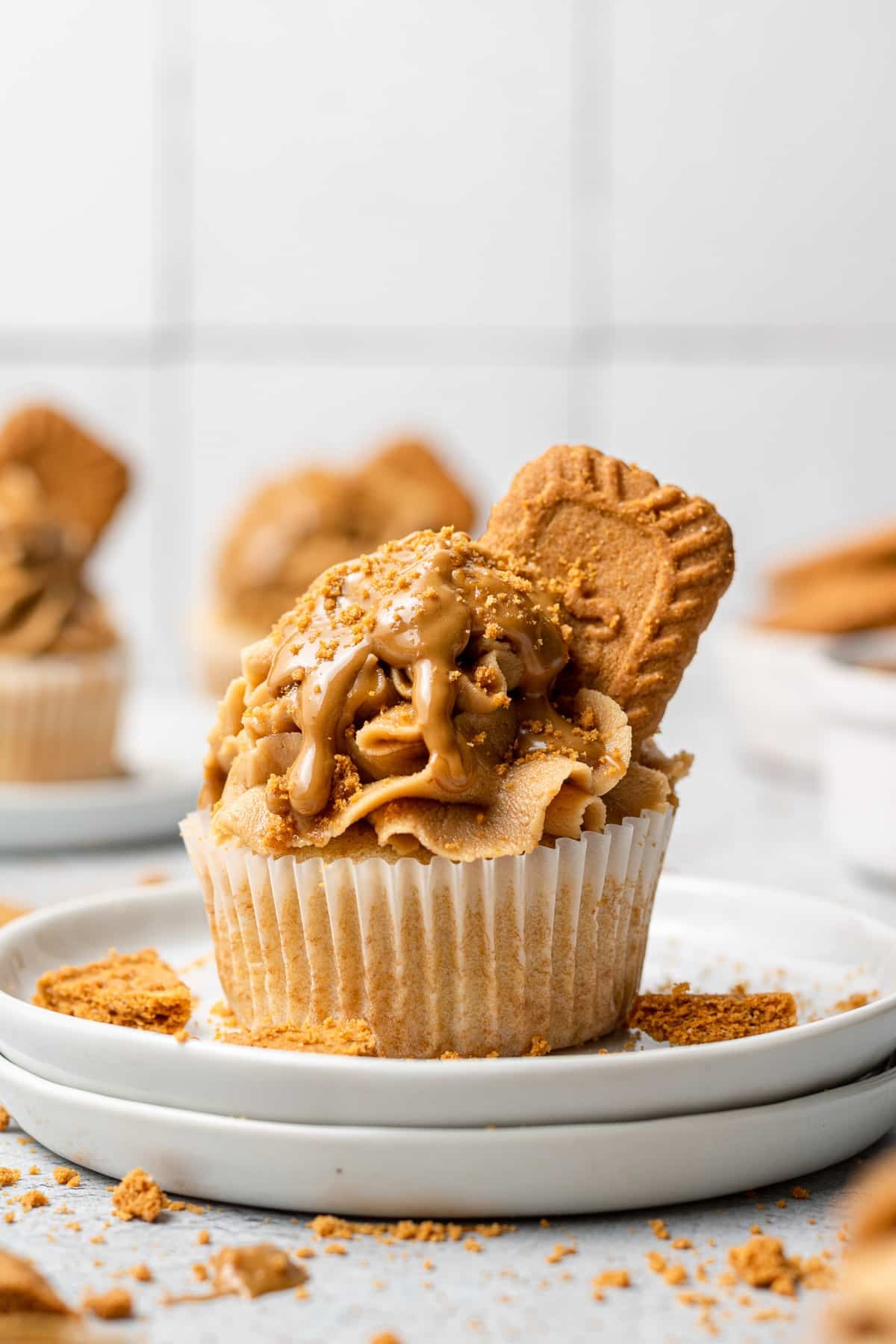 A cupcake topped with a generous swirl of Biscoff buttercream, drizzled with cookie butter, sprinkled with Biscoff cookie crumbs, and garnished with a whole Lotus Biscoff cookie, served on a white plate