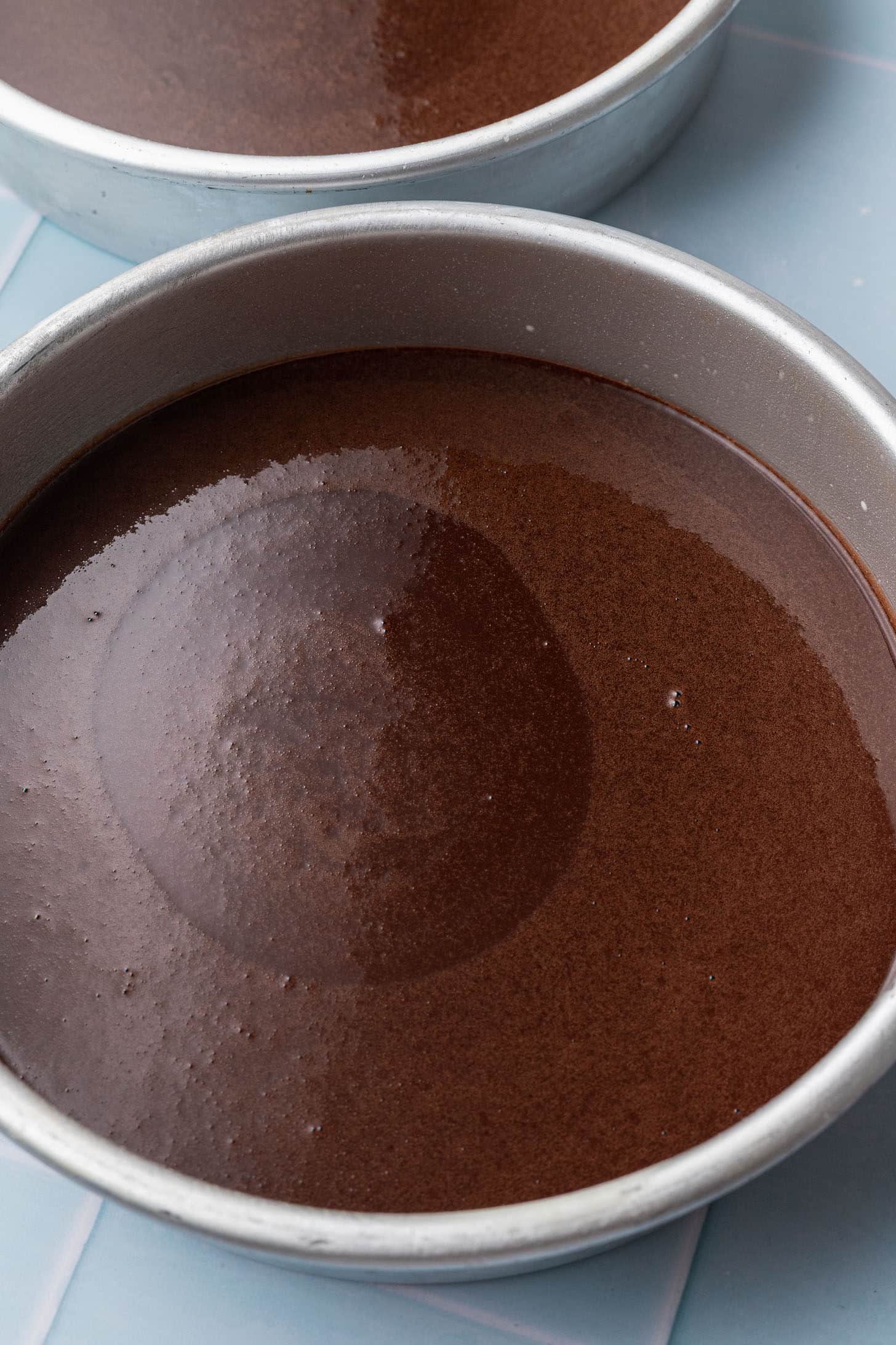 Overhead view of chocolate cake batter divided evenly between two round silver cake pans, ready to go into the oven
